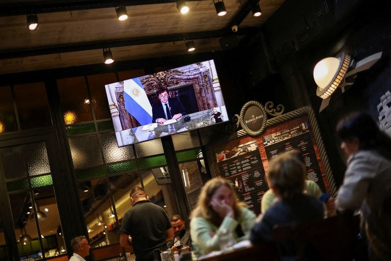 Foto de archivo - Una pantalla muestra al presidente Javier Milei dando un discurso por cadena nacional por televisión, mientras varias personas cenan en un restaurante en Buenos Aires. Abr 22, 2024. REUTERS/Agustin Marcarian