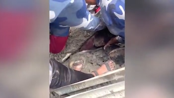 Personal de rescate con uniformes de camuflaje trabaja para sacar a una menor atrapada bajo una masa de lodo