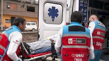 Tres rescatistas con chalecos de SAMU trasladan a una persona en camilla hacia la parte trasera de una ambulancia abierta