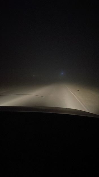 Visto do carro no escuro. Os faróis iluminam a estrada reta coberta por uma névoa espessa. Uma linha branca marca a estrada