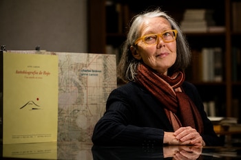 Una mujer con gafas de montura amarilla y bufanda marrón posa junto a dos libros en una mesa reflexiva.