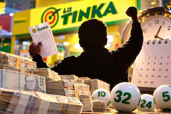 Una persona sostiene un boleto de La Tinka frente a fajos de billetes peruanos, un calendario, un reloj y varias bolillas numeradas