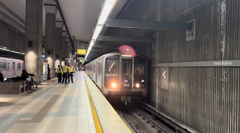 Un tren blanco y gris con luces frontales llega a un andén de la estación Union Station; personas y personal de seguridad se ven en la plataforma