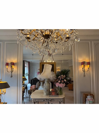 Lámpara de araña de cristal, apliques de pared, mesa consola con jarrón, flores rosas, libros, y un vestido blanco colocado sobre la base de una lámpara