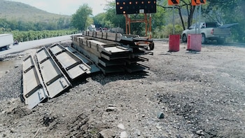 Paneles metálicos de construcción apilados en varias hileras sobre el suelo de tierra en una zona arbolada