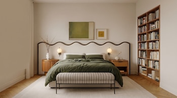 Vista frontal de un dormitorio moderno con una cama de edredón verde oliva, dos mesitas de noche redondas, lámparas de pared y una estantería con libros.