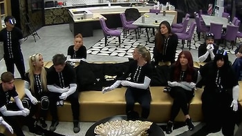 Grupo de personas con vestimenta negra y guantes blancos sentadas en un sillón dentro de una amplia sala
