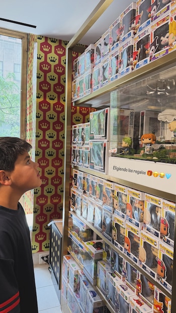 Niño de perfil observa estantes repletos de cajas de figuras coleccionables Funko Pop de diversos personajes, con texto “Eligiendo los regalos”