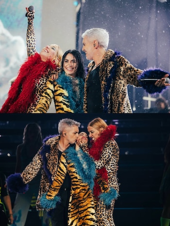 Tres artistas sonriendo en el escenario. Lali con cabello oscuro, una mujer rubia y un hombre con cabello gris. Visten abrigos animal print con plumas de colores