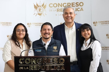 Cuatro personas posan sonriendo frente a un podio con micrófonos y un fondo blanco con varios logotipos que incluyen el texto 'Congreso de la República'