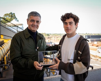 Jorge Macri, de jaqueta verde e gola alta azul, e Franco Colapinto, de cardigã marrom, sorriem enquanto seguram uma modelo na ponte.