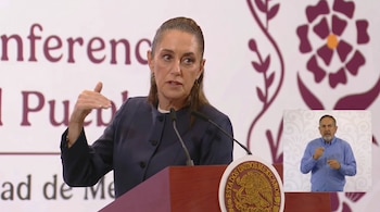Una mujer con blazer azul oscuro habla en un podio de madera con el escudo de México. En un recuadro, un hombre en camisa azul interpreta en lengua de señas.