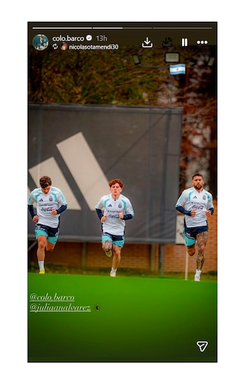 Tres futbolistas con camisetas y pantalones cortos celestes y blancos corren en fila sobre un campo de césped verde. Al fondo se ve una valla oscura