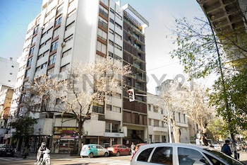 Vista exterior de un edificio alto de apartamentos en una calle urbana, con árboles, coches aparcados y personas en la acera