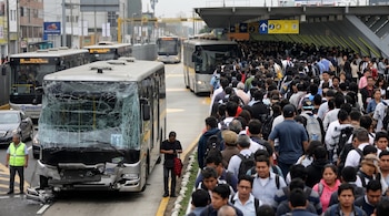 Un autobús Metropolitano con el parabrisas roto y parachoques dañado, junto a una multitud de pasajeros esperando en una estación abarrotada.