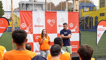 Una mujer habla por micrófono junto a un hombre con brazos cruzados, frente a un banner rojo y blanco con logos de Fundación Empate y Betano, ante una audiencia