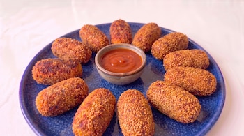 Un plato azul circular con croquetas empanadas en semillas de sésamo y un pequeño recipiente con salsa roja en el centro.
