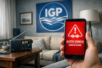 Una mano sostiene un teléfono móvil con una alerta sísmica en pantalla roja. Detrás, una sala de estar con un póster azul del IGP, una radio, un sofá y una lámpara.