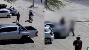Grabación de seguridad de baja resolución mostrando una calle con varios vehículos estacionados, figuras humanas, y una motocicleta en movimiento durante el día
