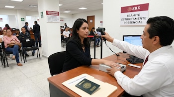 Una mujer sentada frente a un funcionario de la SRE, quien le escanea el iris y captura sus huellas dactilares para el Pasaporte Mexicano en una oficina.