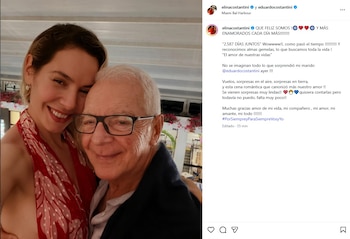 Elina Costantini, una mujer rubia sonriente con un top rojo estampado, abraza a Eduardo Costantini, un hombre mayor con gafas y camisa azul