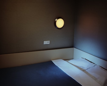 Habitación con paredes marrones, cabecero beige, cama con sábanas azules y almohadas blancas, lámpara redonda amarilla encendida, toma de corriente blanca