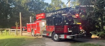 Un camión de bomberos rojo estacionado en un camino rodeado de árboles cerca de una cerca de madera