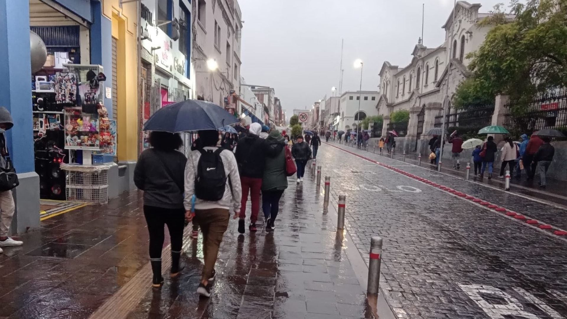 En Arequipa, transeúntes con paraguas y abrigos transitan por las calles mojadas de la ciudad, reflejando el clima lluvioso y nublado que afecta la región. (Andina)