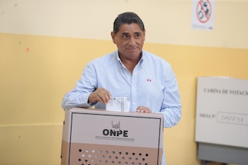 Carlos Álvarez, con camisa a rayas azules y blancas, introduce una papeleta en una urna electoral de la ONPE. Al fondo, se aprecia una cabina de votación