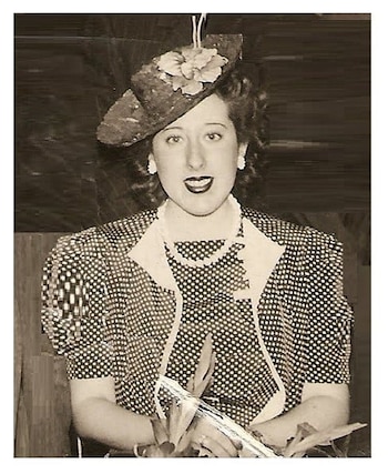 Retrato en tono sepia de Nelly Lainez, una mujer sonriente con cabello oscuro, sombrero con una flor, pendientes blancos, collar de perlas y vestido de lunares