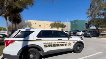 Vista lateral de un SUV policial blanco con la inscripción 'Martin County Sheriff' y rayas verdes y doradas, estacionado bajo un cielo azul