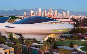 Edificio blanco y futurista del Lucas Museum of Narrative Art con techos de paneles solares y jardines, frente al horizonte de Los Ángeles y montañas