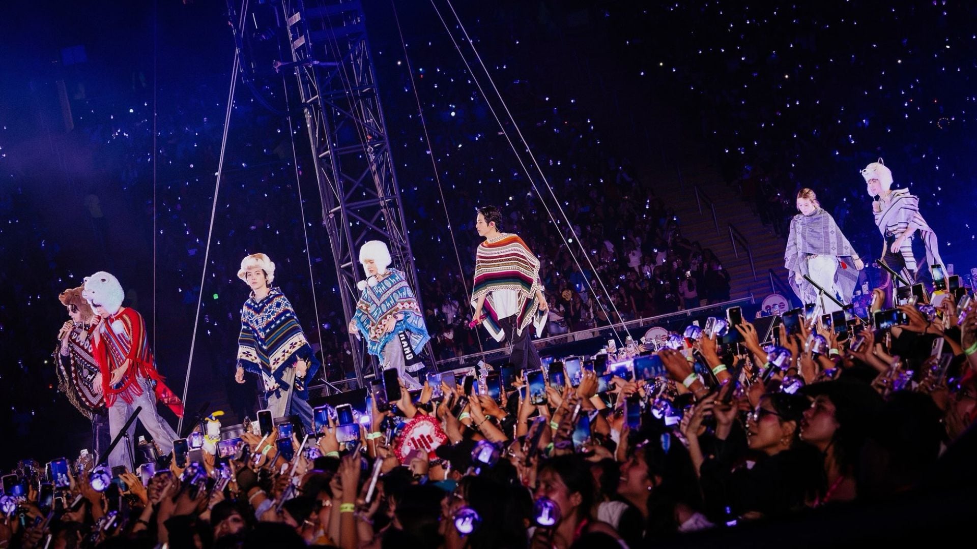 Los integrantes de la agrupación BTS cantan en un escenario con ponchos y chullos ante sus seguidores.