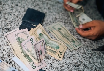 Billetes de dólares estadounidenses, una billetera negra y manos contando dinero sobre una superficie de granito