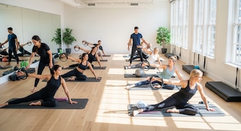 Clase de Pilates grupal con hombres y mujeres en colchonetas, utilizando aros de ejercicio. Dos instructores guían a los participantes.