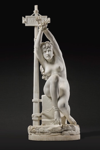 Escultura de mármol blanco de una mujer desnuda atada por las muñecas y los tobillos a un poste vertical, con la palabra 'HYPATIA' grabada en la parte superior