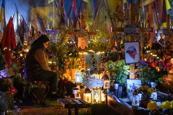 Un familiar enciende velas y lleva flores y banderas a las tumbas de los soldados ucranianos que murieron en la guerra con Rusia el Día de Todos los Santos en el Campo de Marte del cementerio Lychakiv en Lviv, Ucrania, el viernes 1 de noviembre de 2024. (Foto AP/Mykola Tys)