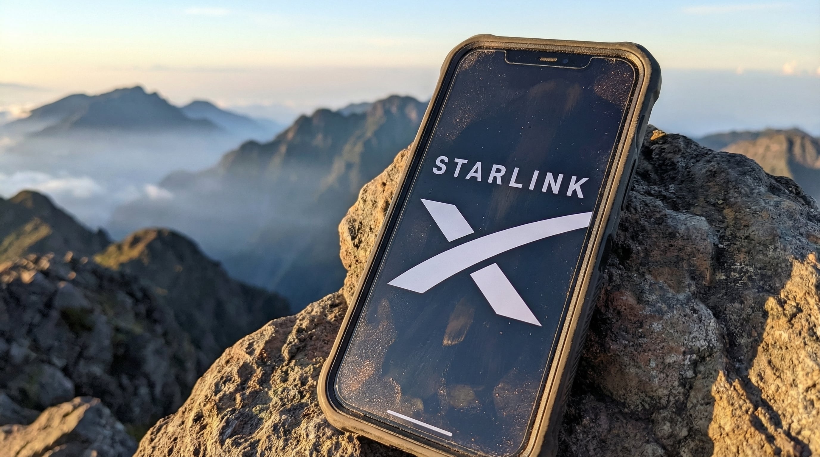 El logo de Starlink se muestra en un teléfono móvil sobre una roca, con un impresionante paisaje montañoso cubierto de niebla de fondo al amanecer. (Imagen Ilustrativa Infobae)