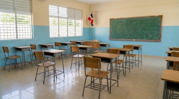 Interior de un salón de clases limpio y vacío en República Dominicana con paredes bicolor, pupitres de madera y metal, una pizarra y la bandera dominicana.