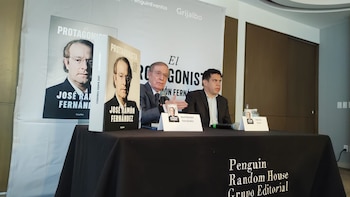 José Ramón Fernández, un hombre mayor con gafas, habla en un micrófono en un evento. A su lado, otro hombre y copias de su libro 'El Protagonista' en una mesa