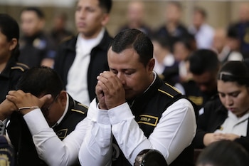 Hombre con camisa blanca y chaleco oscuro con el distintivo '63783-P', manos juntas frente al rostro, rodeado de otras personas uniformadas