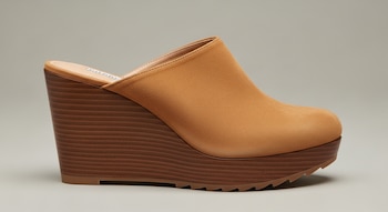 Una sandalia de cuña moderna color camel en gamuza, con puntera redondeada, cuña de madera oscura y suela tipo track, sobre un fondo gris claro.