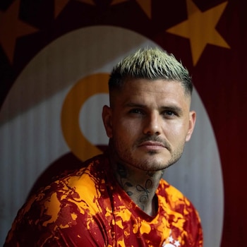 Primer plano de Mauro Icardi, un hombre con cabello rubio platino corto y barba, vistiendo una camiseta roja y naranja. Fondo con el logo de Galatasaray