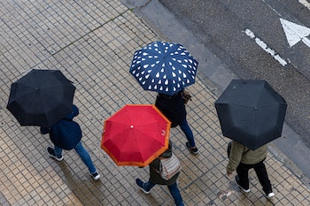 Varias personas se protegen de la lluvia con paraguas en Zaragoza. (Javier Belver/EFE)