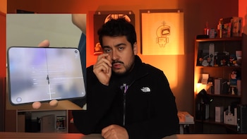 Un hombre sentado frente a la cámara junto a una imagen sobrepuesta de un teléfono plegable con una línea oscura en el centro de la pantalla