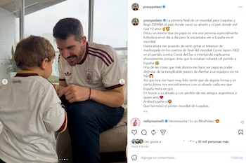 Un hombre y un niño sentados. Ambos visten camisetas de fútbol de la selección de España. El hombre mira al niño sonriendo y el niño le da la espalda a la cámara