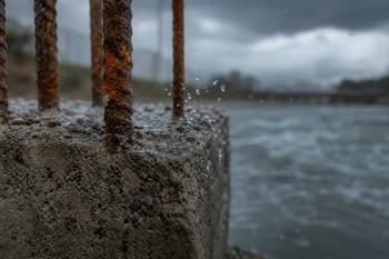 Un bloque de concreto rugoso con varillas de hierro oxidadas y gotas de agua en la superficie frente a un río desenfocado.