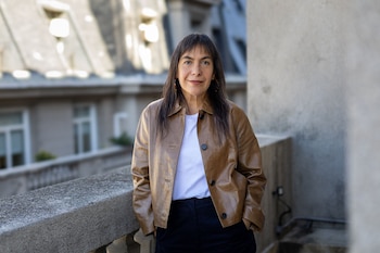 Retrato de Tania Candiani, mujer de cabello oscuro y largo, con chaqueta de cuero marrón, camiseta blanca y pantalón oscuro, en un balcón