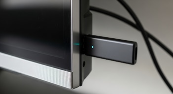 Memoria USB negra conectada a puerto lateral de televisor negro con borde inferior plateado, con luz azul encendida en la USB.