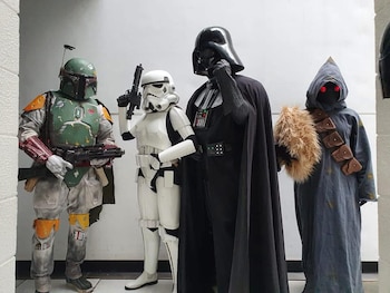 Cuatro personas en cosplay de Star Wars: Boba Fett (izquierda), un Stormtrooper, Darth Vader con su máscara y un Jawa (derecha) posan de pie